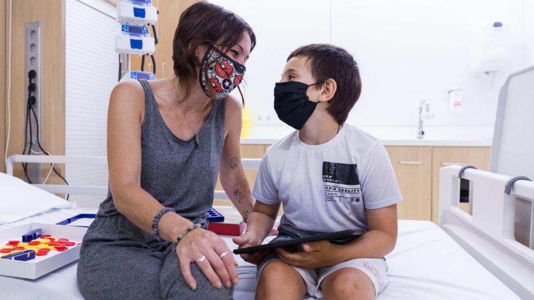 Una madre mira a su hijo en un box del Hospital de día del SJD Pediatric Cancer Center