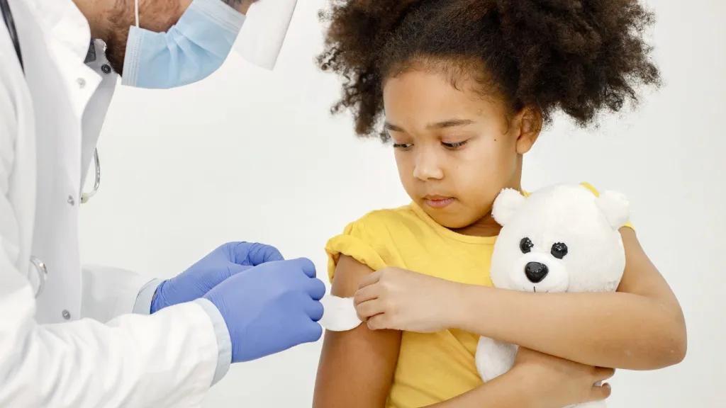 Girl receiving vaccine in arm with teddy bear Girl receiving vaccine in arm with teddy bear